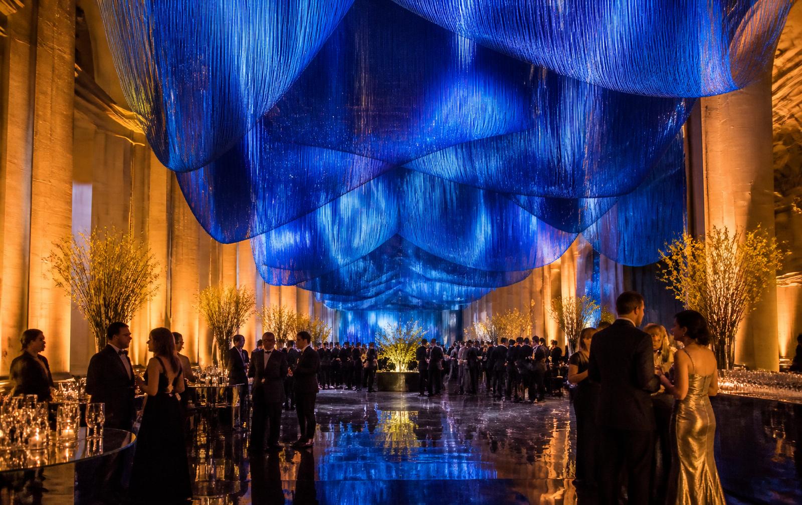 Banquet hall under a cascading blue silk canopy with golden uplit columns